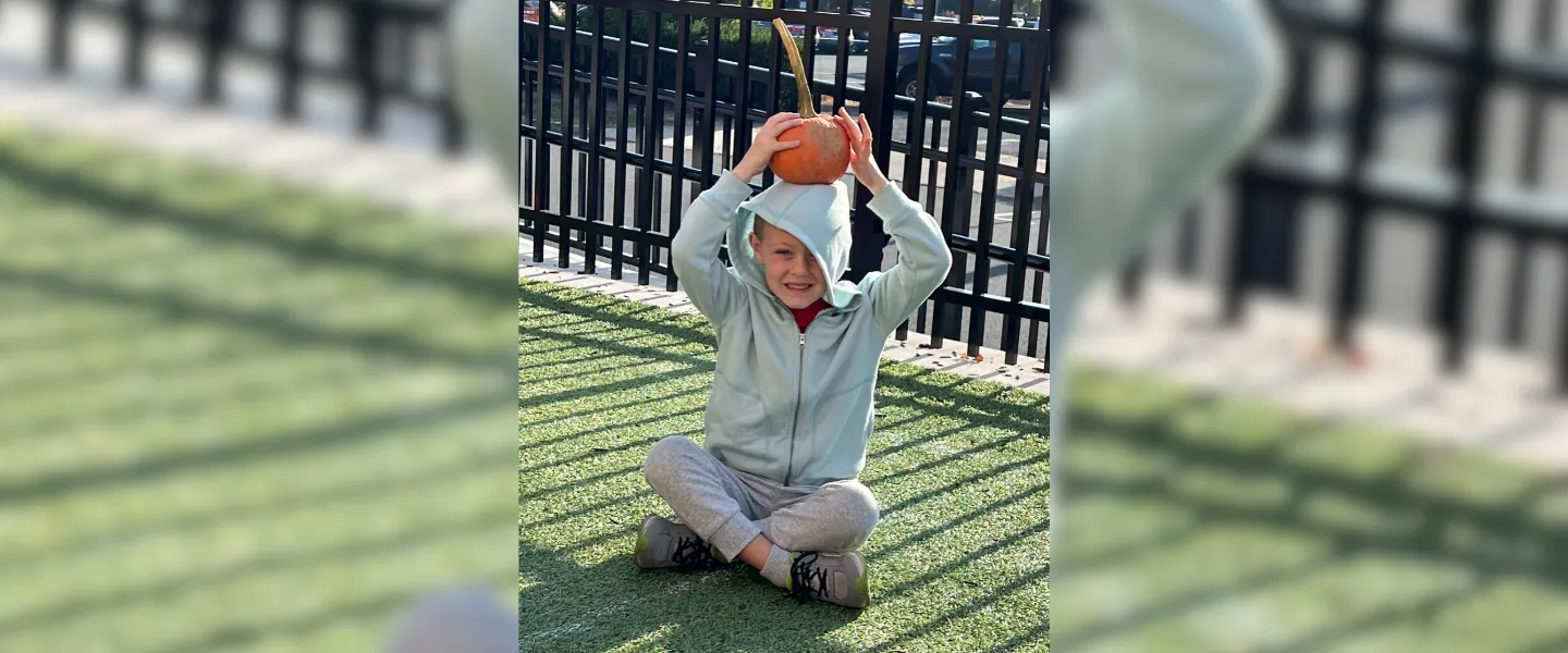 Smiling student balancing pumpkin on their head